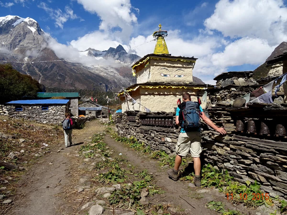 Tourirsts walk by a Buddhist a monument at Samagaun in Manaslu Trekking Trail