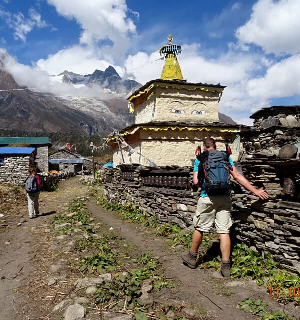 Trekkers walk by religius shrine at Samagaun in Manaslu Circuit Nepal